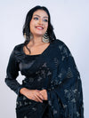 Woman wearing a black saree with white patterns on a plain background